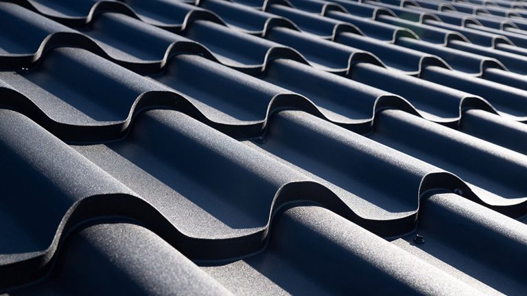 Close-up of dark gray, wavy roof tiles reflecting sunlight in a repeating pattern.