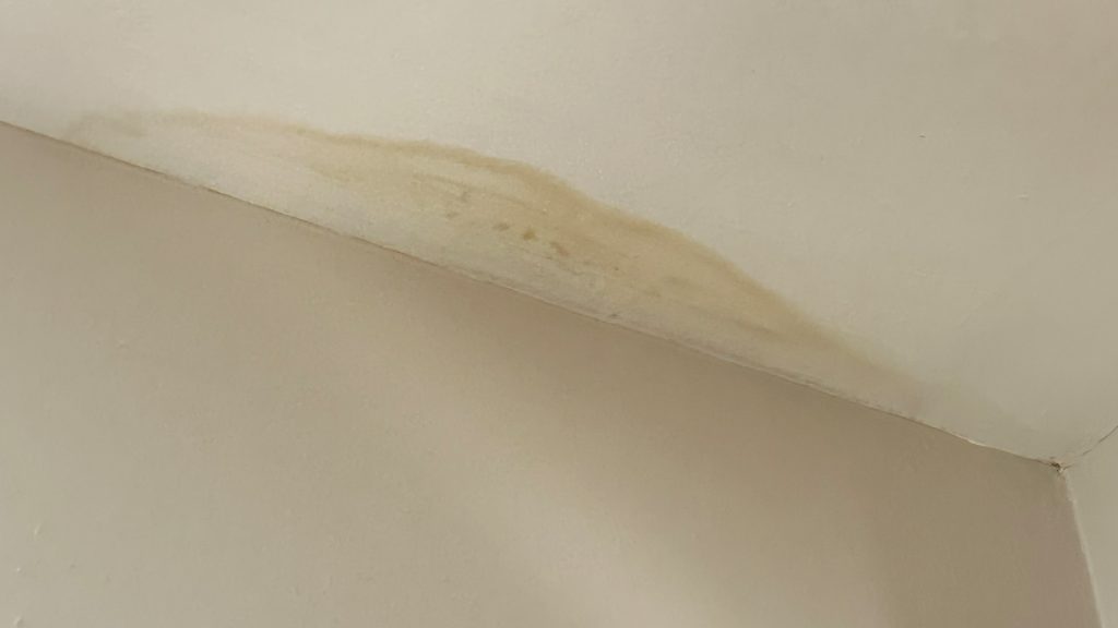 Beige interior wall with a brown water-stain streak along the ceiling joint.