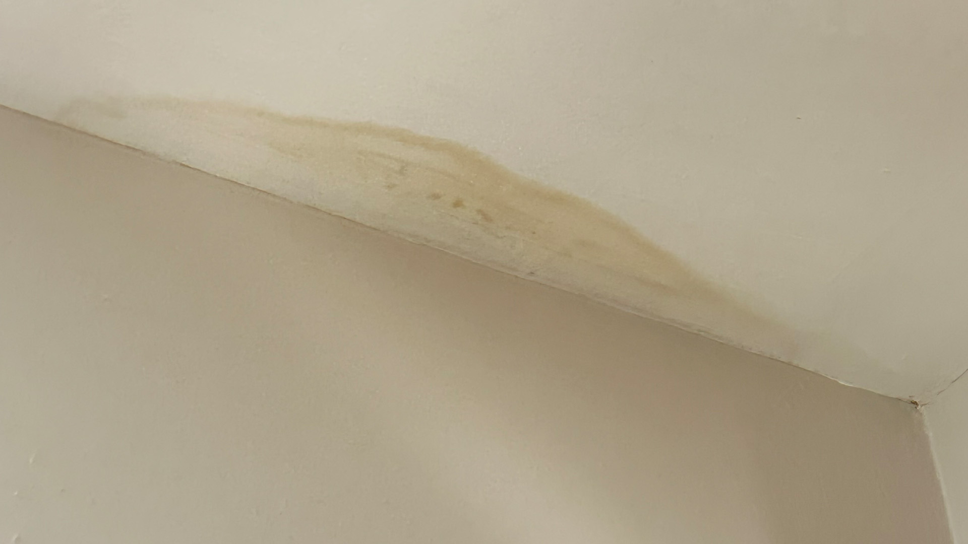 Beige interior wall with a brown water-stain streak along the ceiling joint.
