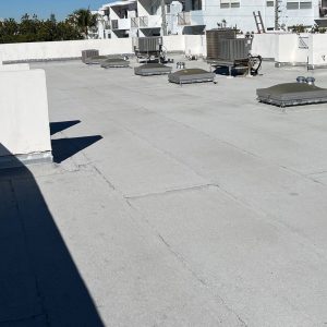 Flat white rooftop with multiple HVAC condensers and vents, blue sky and surrounding buildings in the background