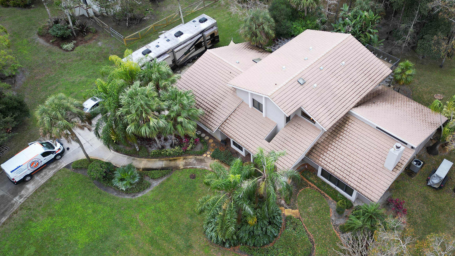 Aerial view of a beige-roofed house with palm trees, curved walkway, and an ambulance on the driveway.