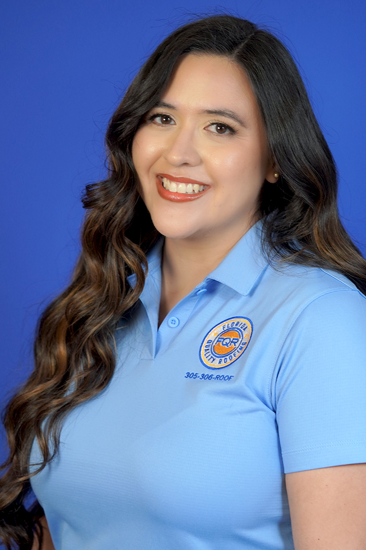 Smiling woman with long wavy hair in a light blue polo shirt with a circular logo on the chest, against a blue backdrop.