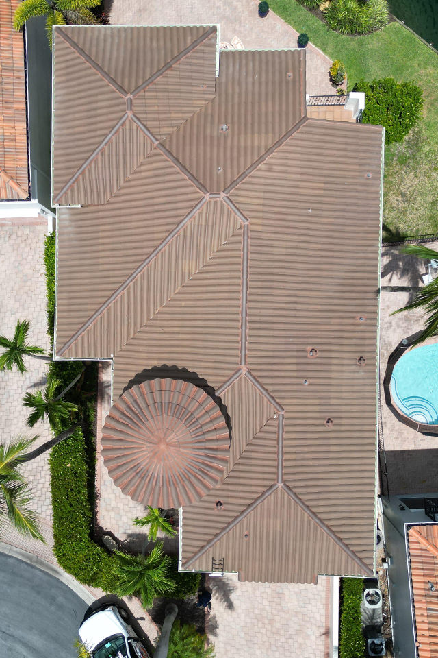 Aerial view of a brown tiled roof with a circular turret, surrounding patio, palms, and a kidney-shaped pool to the right.