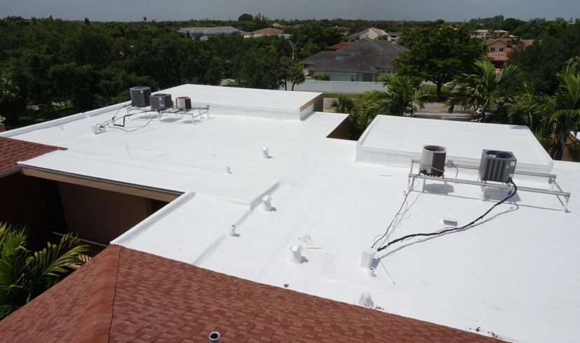 White flat rooftop with two outdoor air conditioning units and exposed wiring, overlooking a residential neighborhood with trees in the distance.